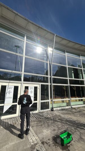 A man using an extended pole squeegee to clean a high exterior window.